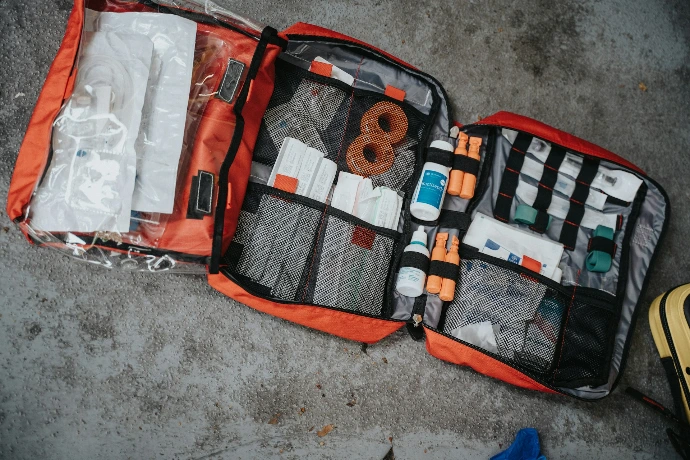 An open red medical bag filled with various supplies on a grey surface