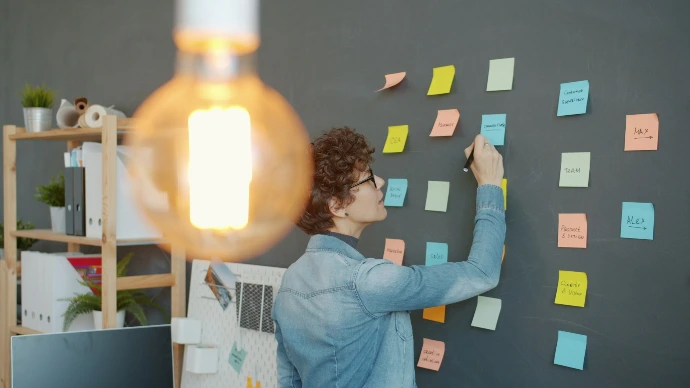 Person writing on colorful sticky notes on wall.